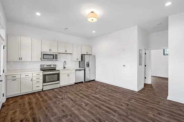 a kitchen with granite countertop a refrigerator oven a sink dishwasher and white cabinets with wooden floor