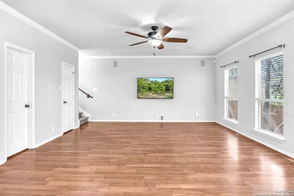 an empty room with wooden floor chandelier fan and windows