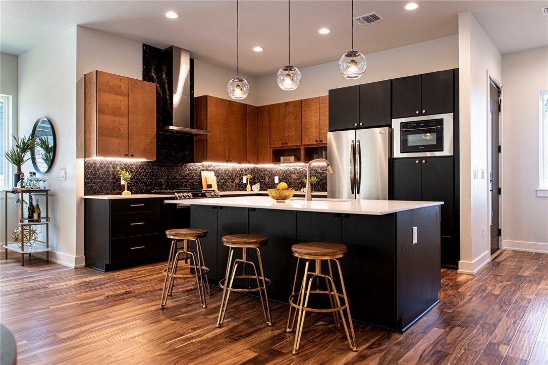 a kitchen with stainless steel appliances kitchen island granite countertop a refrigerator a stove a sink and a dining table with wooden floor