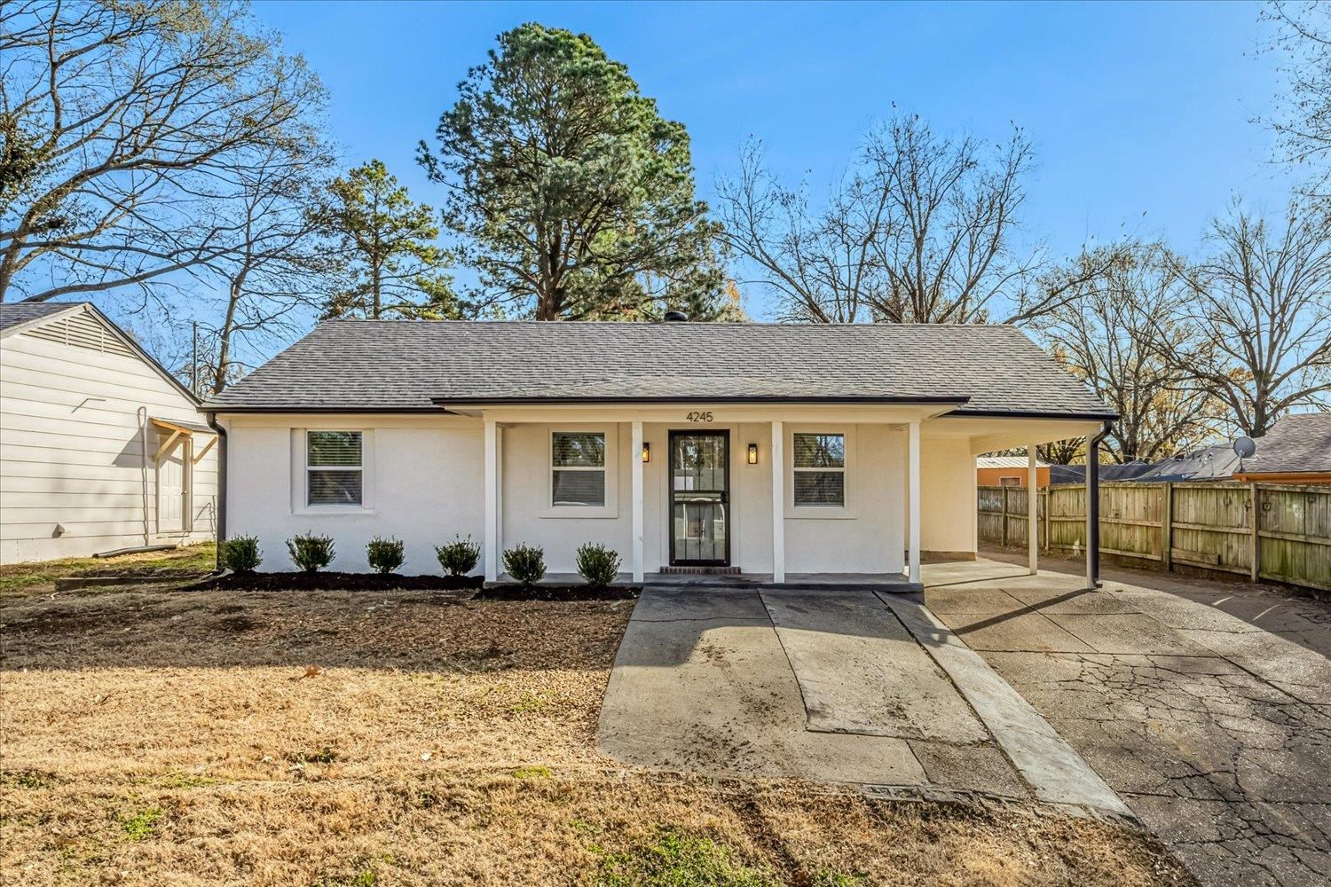 Single story home featuring a shingled roof, a porch, stucco siding, driveway, and a carport