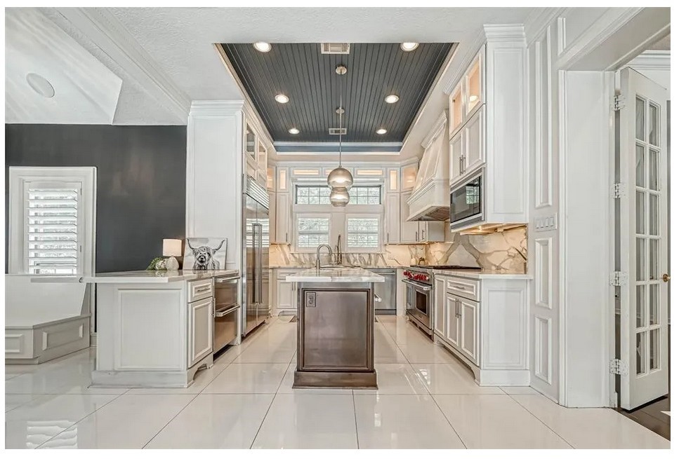 263 Wood Loop Street Houston, TX 77015 - Photo 20 of 45 This kitchen features elegant white cabinetry, a marble backsplash, and modern stainless steel appliances. It includes a central island with pendant lighting, a built-in oven, and a cozy breakfast nook with a window seat, creating a bright and inviting space.