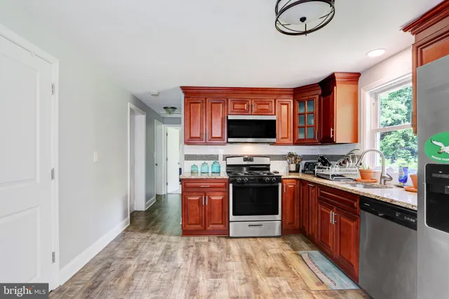 a kitchen with stainless steel appliances granite countertop a stove top oven a sink dishwasher a dining table and chairs with wooden floor