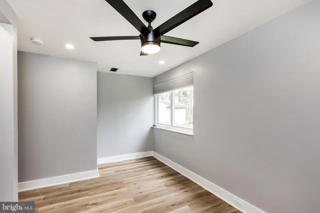 an empty room with wooden floor ceiling fan and windows