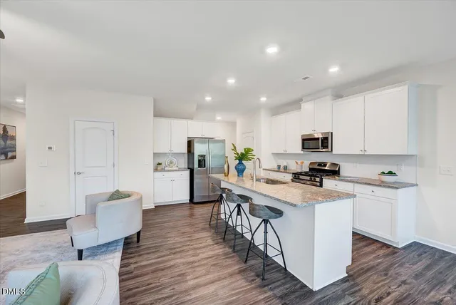 a kitchen with stainless steel appliances a stove a sink a refrigerator white cabinets and wooden floor