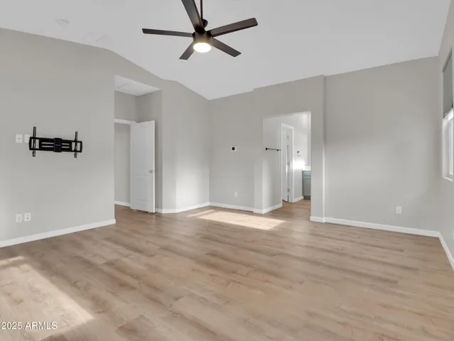 an empty room with wooden floor ceiling fan and windows