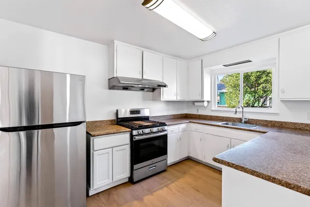 a kitchen with stainless steel appliances granite countertop a stove a sink dishwasher and a refrigerator with wooden floor