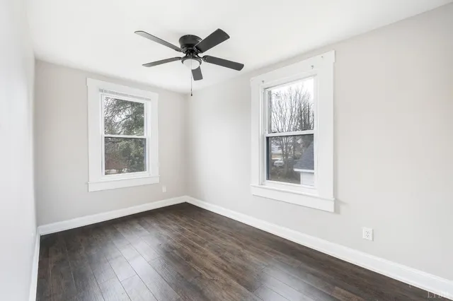 an empty room with wooden floor ceiling fan and window