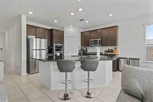 a kitchen with stainless steel appliances kitchen island granite countertop a refrigerator a stove a sink a dining table and chairs