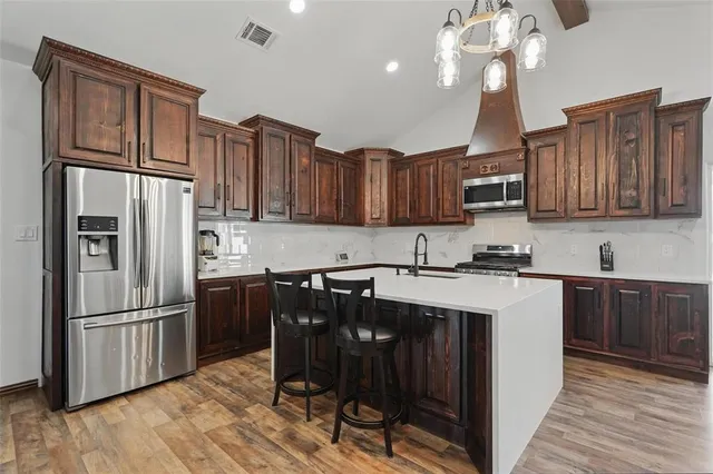 a kitchen with stainless steel appliances granite countertop a refrigerator a sink dishwasher a stove kitchen island and chairs with wooden floor