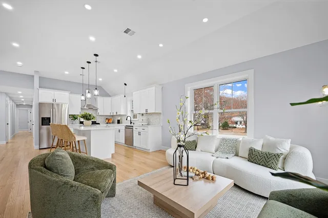 a living room with kitchen couches and kitchen view with wooden floor