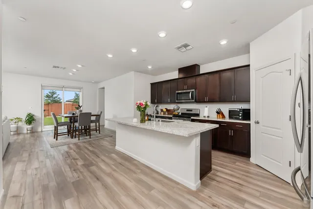 a kitchen with stainless steel appliances a stove top oven a sink dishwasher and a refrigerator with wooden floor