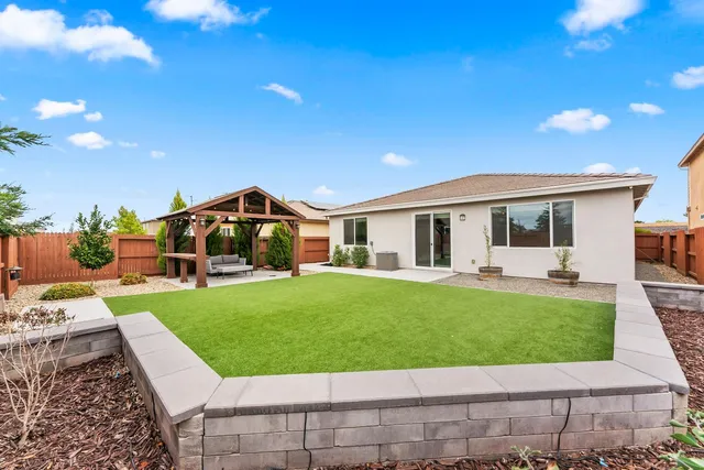 a view of a white house in front of a big yard with plants and large trees