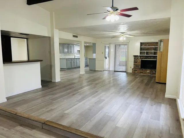 a view of empty room with wooden floor and kitchen view