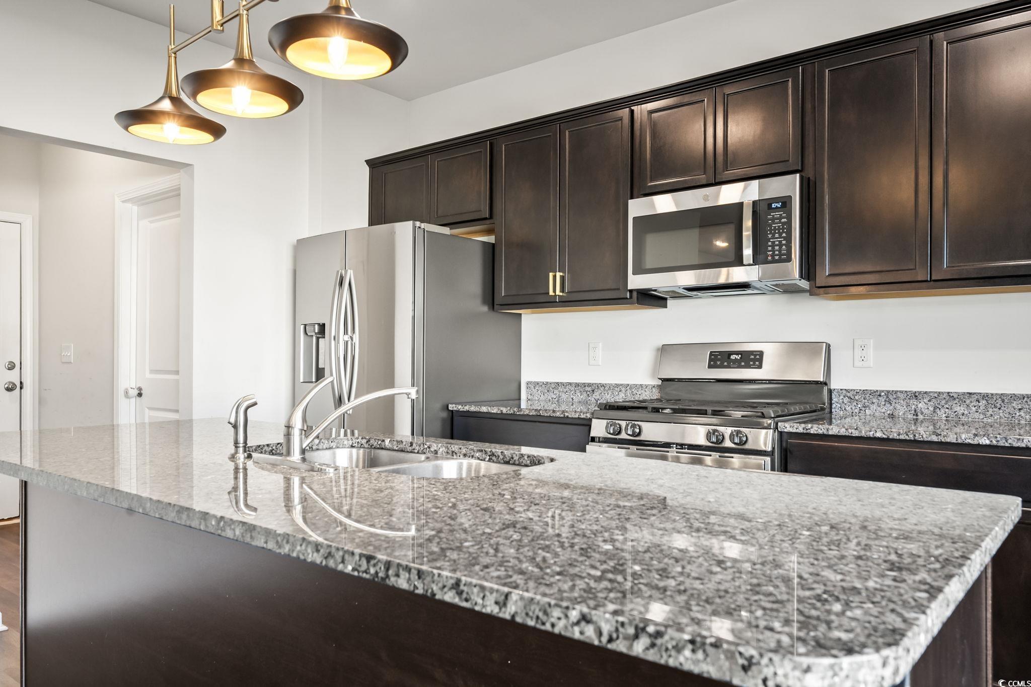 733 Lambeth Lane Conway, SC 29526 - Photo 14 of 40 Kitchen featuring dark brown cabinetry, appliances with stainless steel finishes, light stone counters, and hanging light fixtures