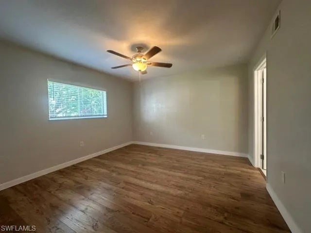 an empty room with wooden floor ceiling fan and windows