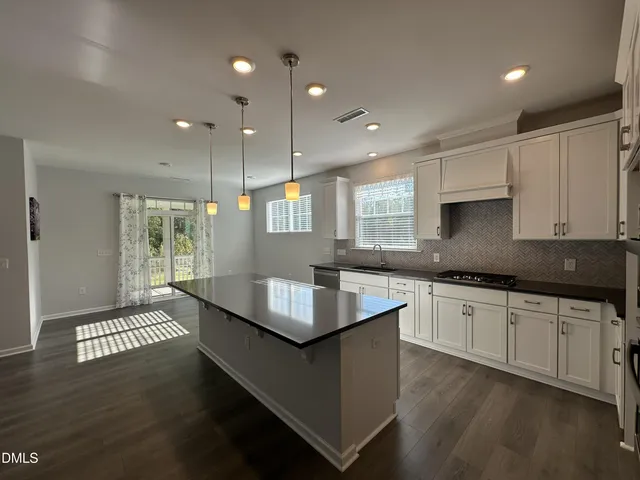 a kitchen with granite countertop a stove a sink a refrigerator and white cabinets with wooden floor