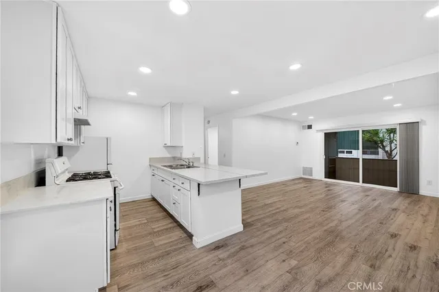 a kitchen with stainless steel appliances granite countertop a stove top oven a sink dishwasher and a refrigerator with wooden floor