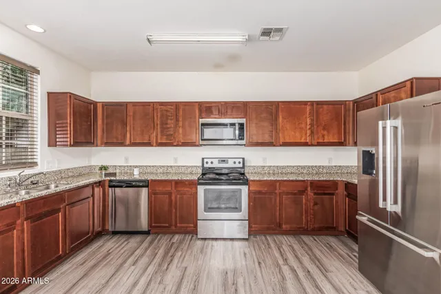a kitchen with stainless steel appliances granite countertop wooden cabinets a sink dishwasher a stove and a refrigerator