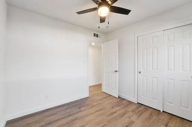 an empty room with wooden floor ceiling fan and window