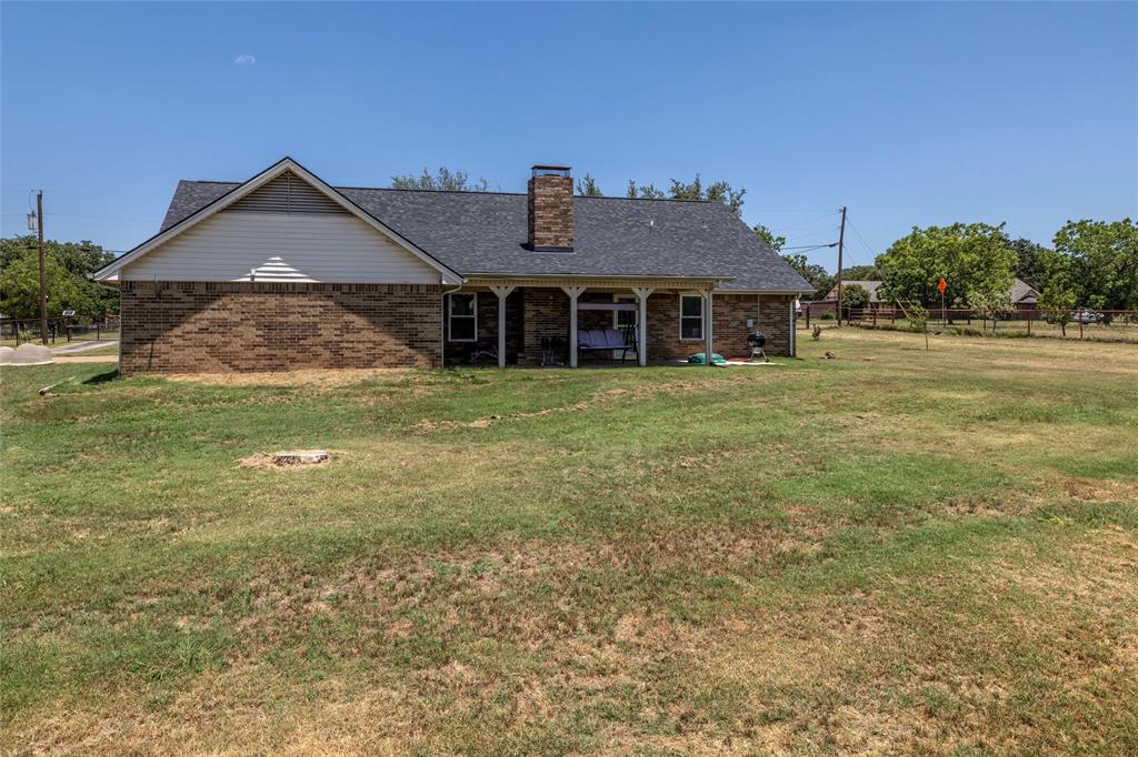 151 County Road 3699 Springtown, TX 76082 - Photo 3 of 35 Brick exterior home featuring a covered back porch with white columns, dark shingle roofing, and a prominent brick chimney