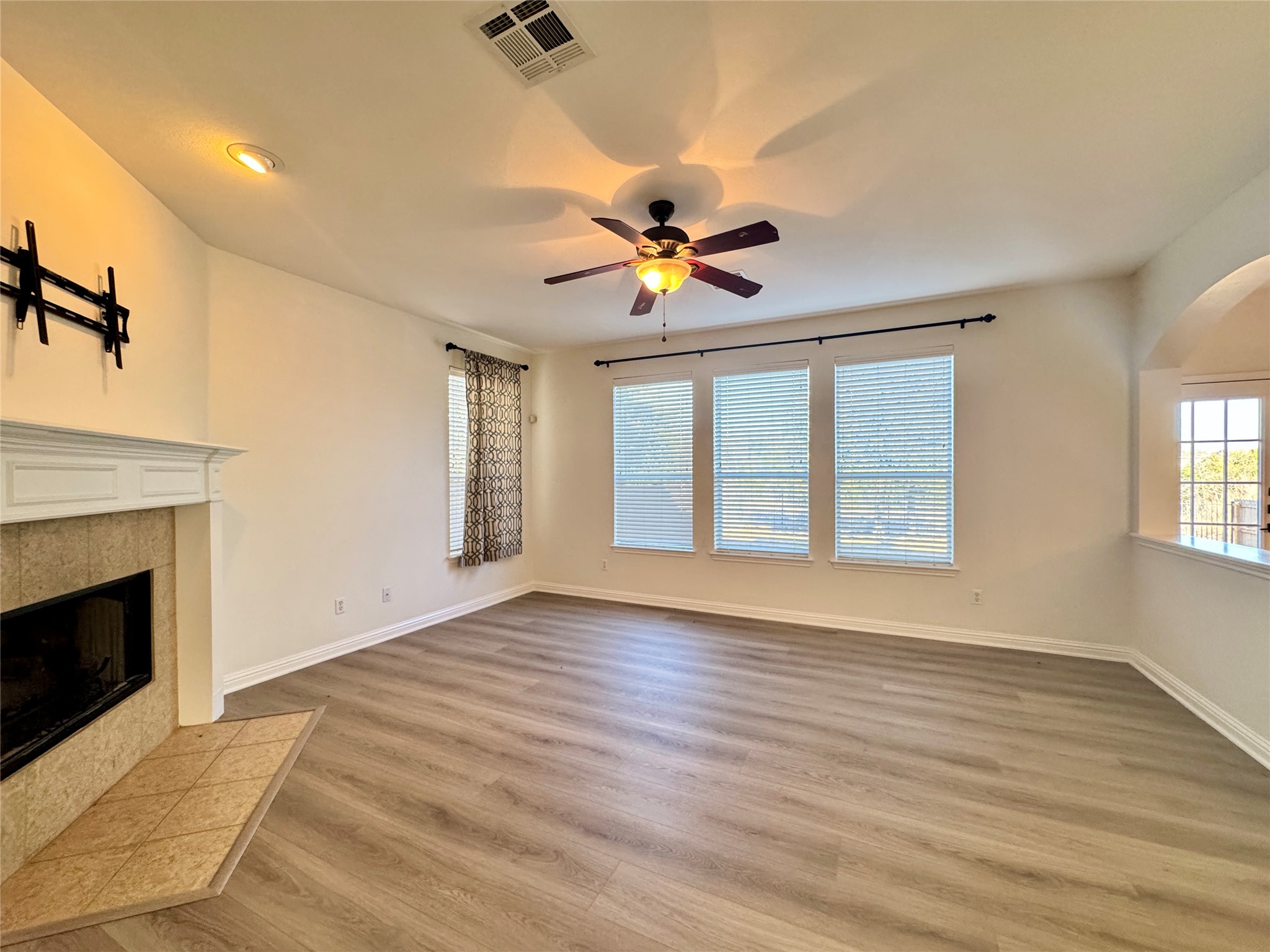 3640 Fossilwood Way Round Rock, TX 78681 - Photo 6 of 19 Unfurnished living room featuring a tile fireplace, light wood-style flooring, ceiling fan, and arched walkways