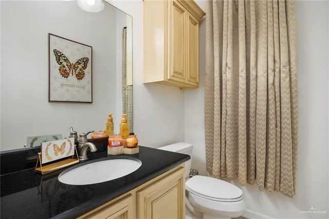 a bathroom with a granite countertop sink a toilet a mirror and shower curtain