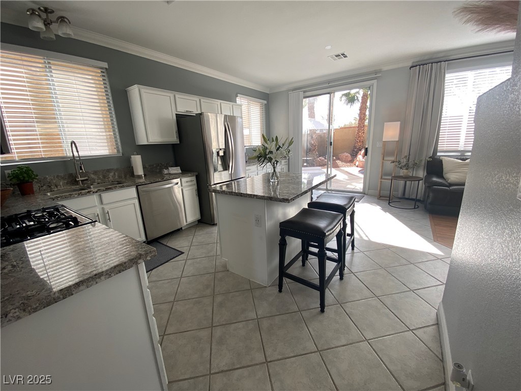 10637 Amblewood Avenue Las Vegas, NV 89144 - Photo 22 of 32 Kitchen with ornamental molding, white cabinetry, a center island, light tile patterned floors, and dark stone counters
