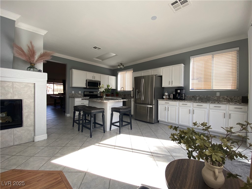 10637 Amblewood Avenue Las Vegas, NV 89144 - Photo 23 of 32 Kitchen featuring ornamental molding, white cabinets, stainless steel appliances, a kitchen breakfast bar, and a fireplace