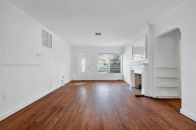 an empty room with wooden floor fireplace and windows