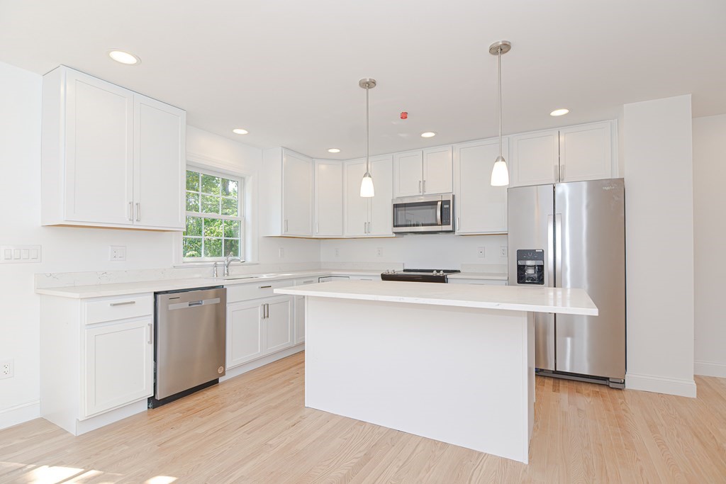 a kitchen with stainless steel appliances a refrigerator a sink dishwasher a stove and white cabinets with wooden floor