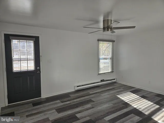 an empty room with wooden floor ceiling fan and windows