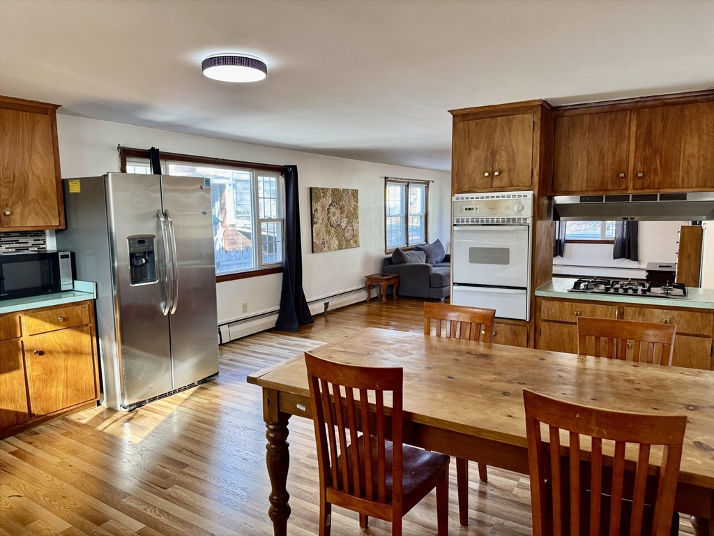156 Nichols Avenue, Unit 1 Watertown, MA 02472 - Photo 6 of 26 a dining hall with stainless steel appliances granite countertop a stove a kitchen island a dining table and chairs with wooden floor