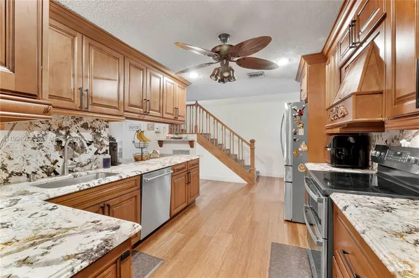a kitchen with stainless steel appliances granite countertop a sink a stove top oven a chimney cabinets and wooden floor