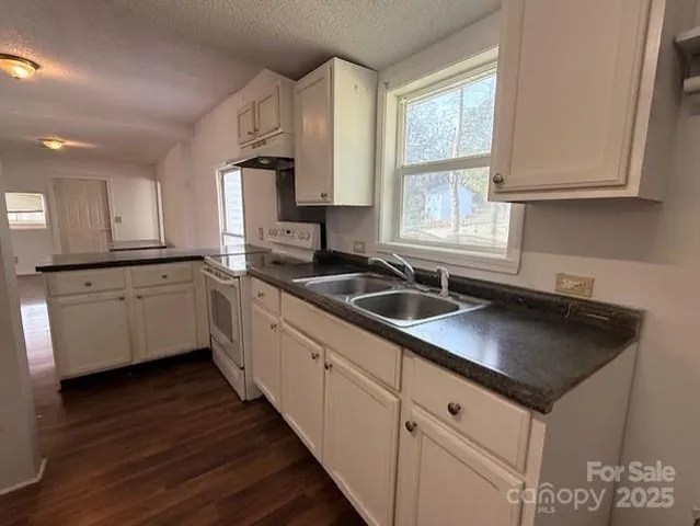 a kitchen with granite countertop a sink dishwasher a stove and white cabinets with wooden floor