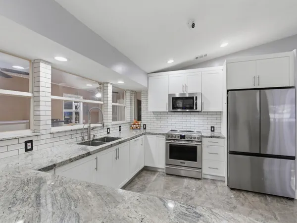 a large kitchen with stainless steel appliances granite countertop a stove a sink a refrigerator a microwave and white cabinets