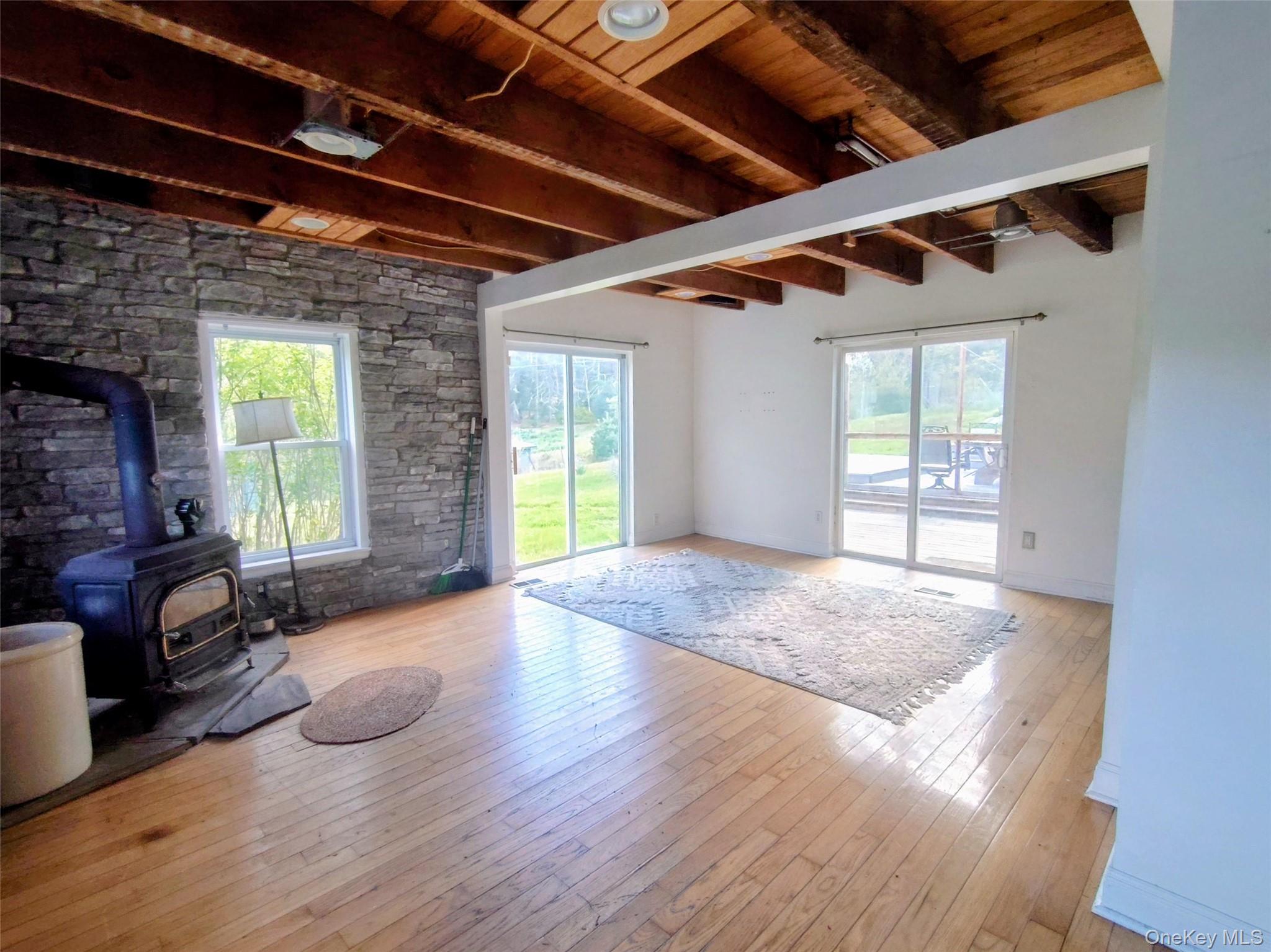 983 Plank Road Forestburgh, NY 12777 - Photo 16 of 50 Interior room with exposed wood beam ceiling, natural wood flooring, a stone accent wall, and a freestanding wood-burning stove