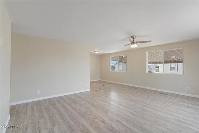 an empty room with wooden floor chandelier fan and windows