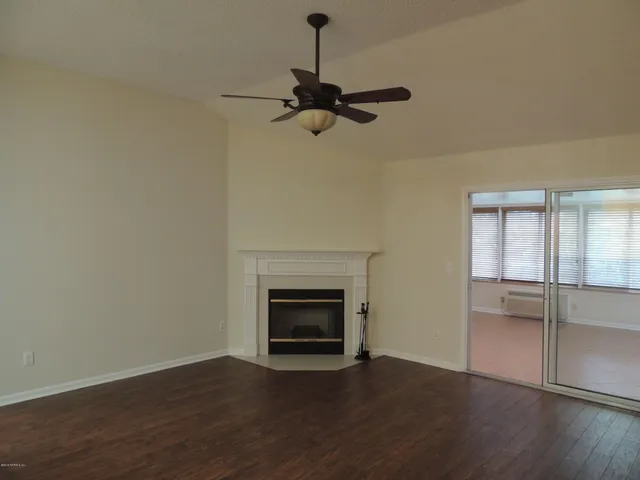 a view of an empty room with wooden floor fireplace and a window