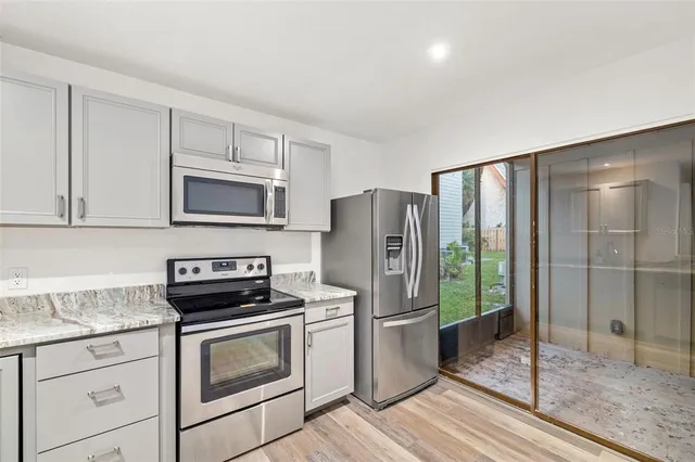 a kitchen with stainless steel appliances granite countertop a refrigerator a stove a sink and white cabinets with wooden floor