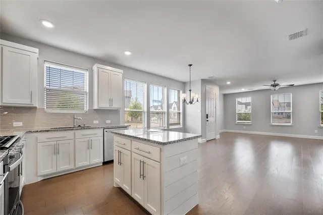 a large white kitchen with granite countertop a sink and dishwasher a stove with wooden floors