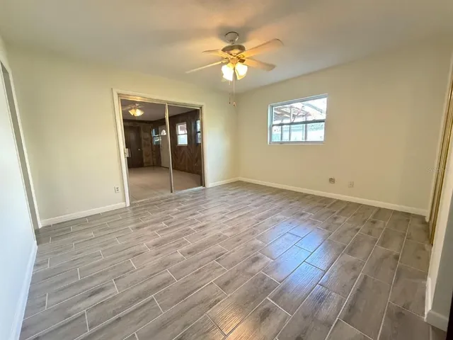 an empty room with wooden floor fan and windows