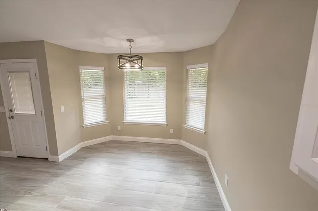 an empty room with chandelier fan and windows