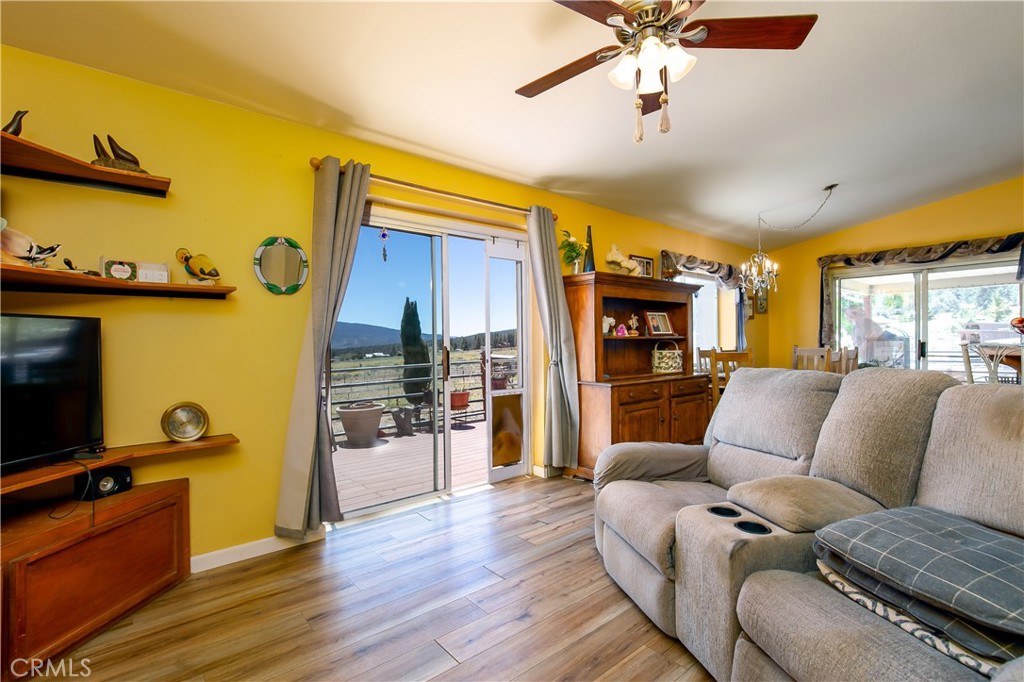 10960 Steinhoff Road Frazier Park, CA 93225 - Photo 23 of 46 An open-concept living space showcasing a cozy seating arrangement and rich wood-look flooring. A vibrant warm accent wall complements the light-filled layout, while massive sliding glass doors frame scenic property views and provide effortless access to the expansive outdoor viewing deck.