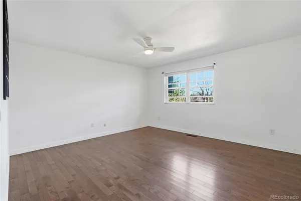 an empty room with wooden floor ceiling fan and windows
