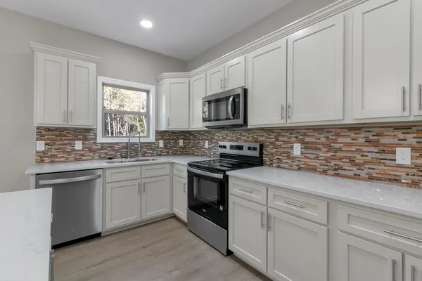 a kitchen with white cabinets appliances a sink and a window