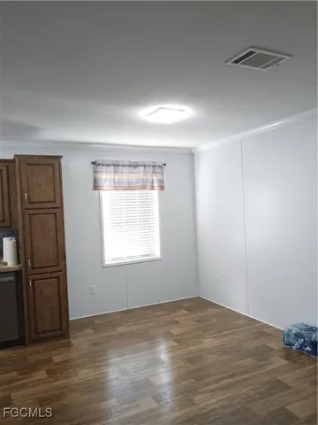 an empty room with wooden floor kitchen view and windows