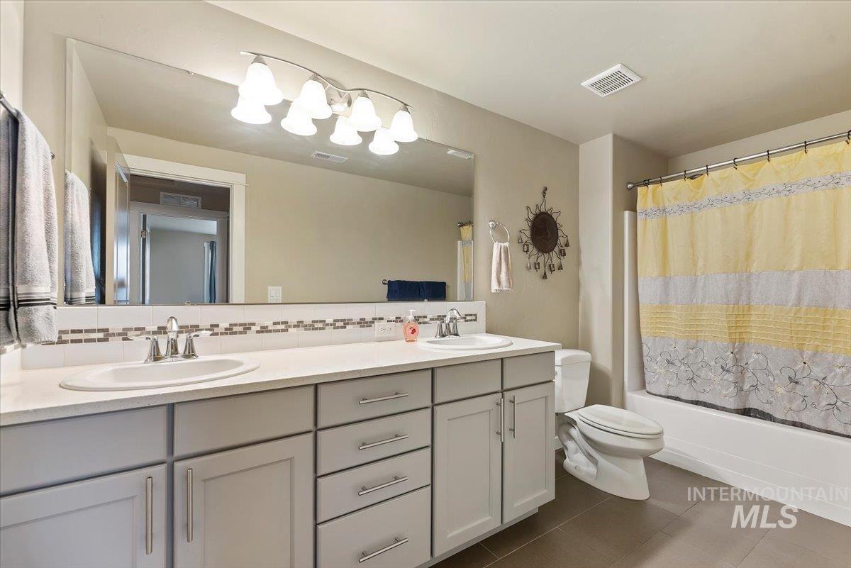 1011 West Riodosa Drive Meridian, ID 83642 - Photo 22 of 38 Full bathroom featuring double vanity, decorative backsplash, shower / tub combo, and dark tile patterned flooring
