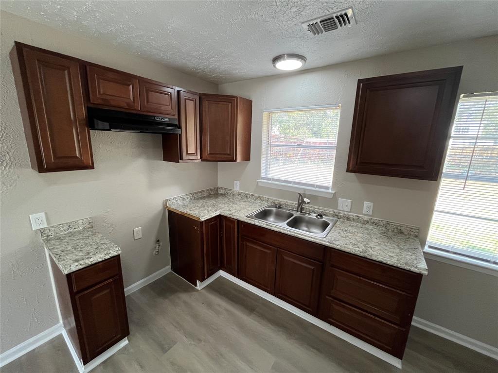 14207 Cimarron Drive Balch Springs, TX 75180 - Photo 5 of 23 Kitchen with a textured wall, light countertops, light wood-type flooring, a textured ceiling, and under cabinet range hood