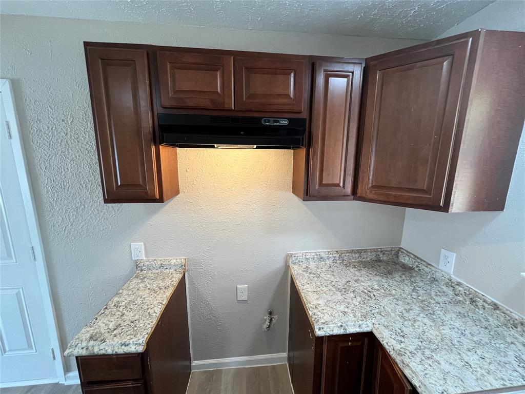 14207 Cimarron Drive Balch Springs, TX 75180 - Photo 6 of 23 Kitchen with a textured wall, wood finished floors, dark brown cabinetry, under cabinet range hood, and a textured ceiling