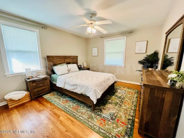a bedroom with a bed a dresser and potted plants with the wooden floor